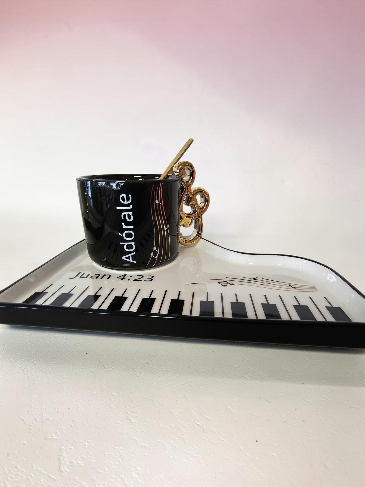 Set de taza negra Libreria Wow con asa de clave de sol dorada y bandeja en forma de piano con teclas y pentagrama.