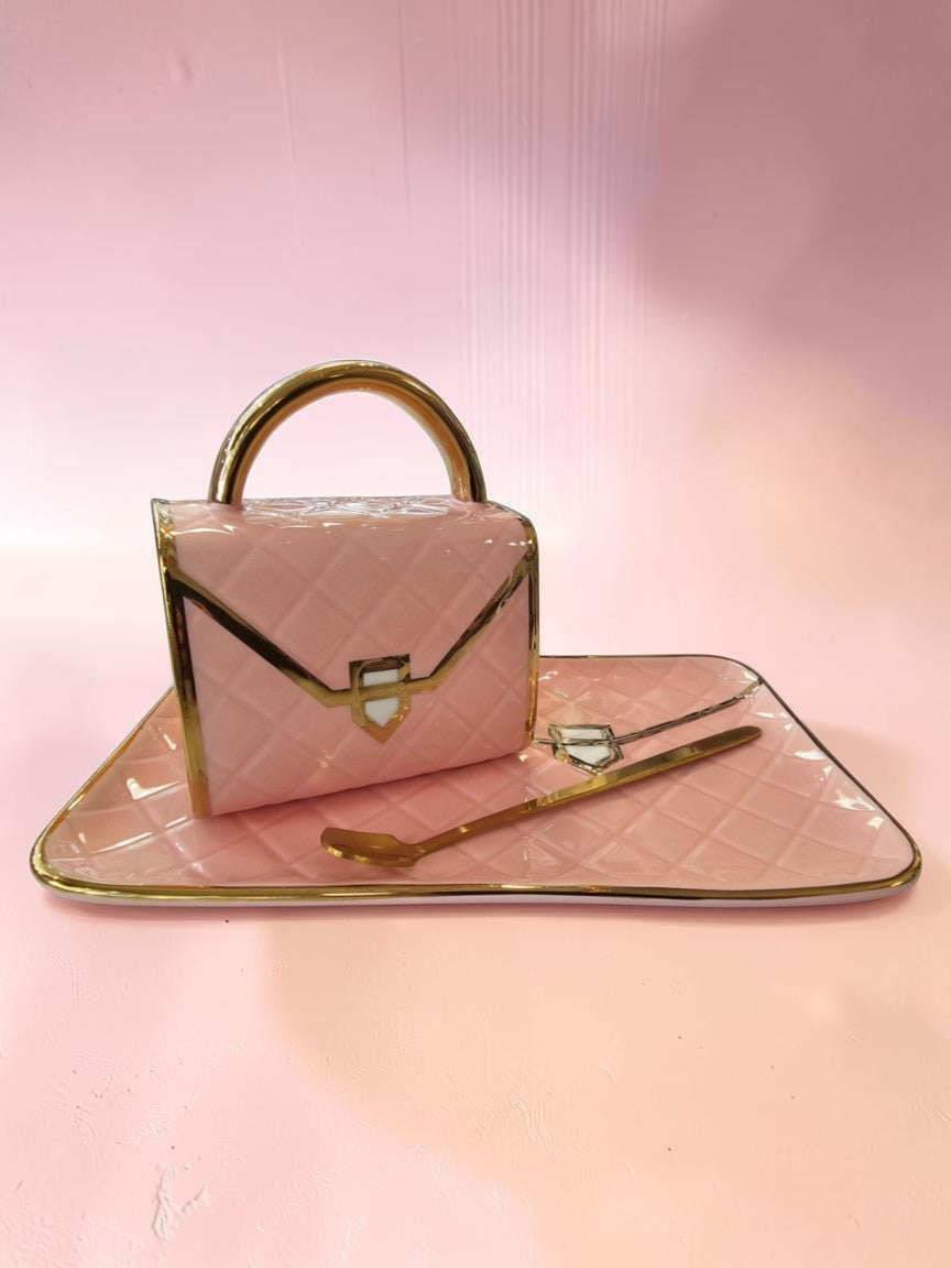 Set de taza y plato Libreria Wow rosa pastel con diseño de bolso acolchado, detalles dorados y cuchara a juego.